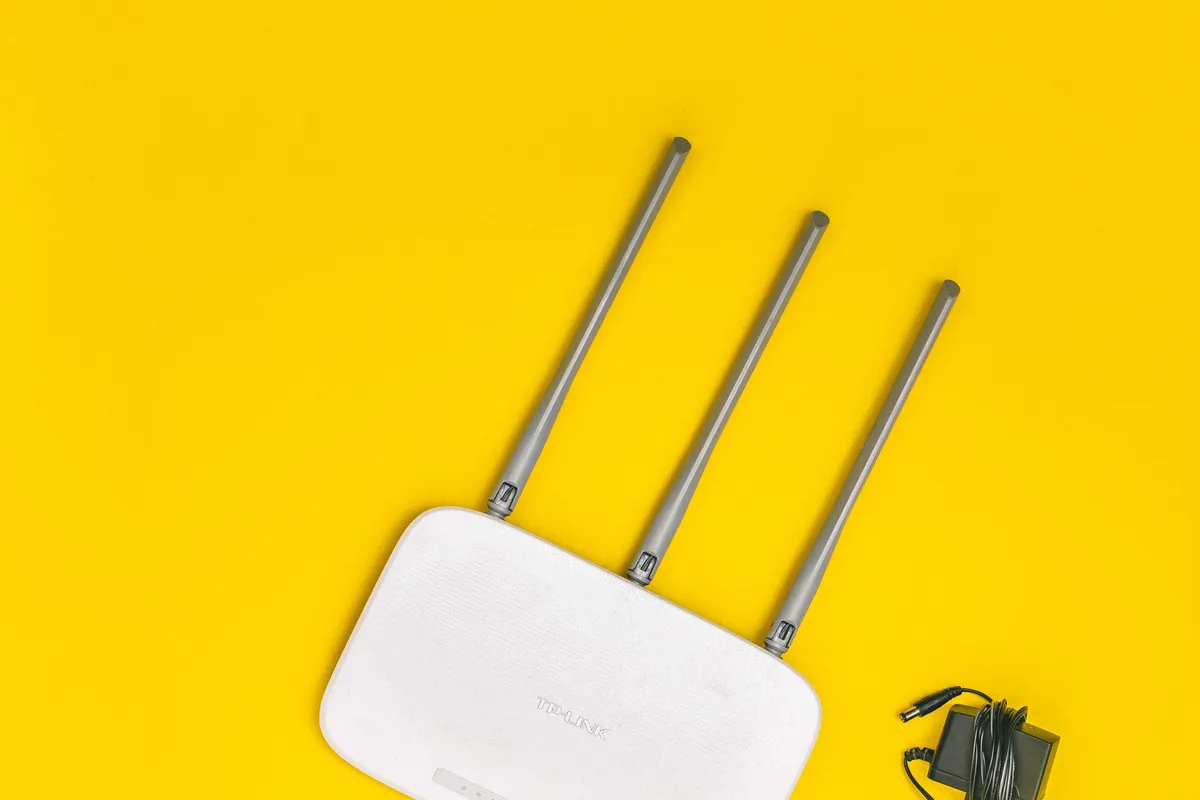 Roteador Wi-Fi branco com três antenas sobre fundo amarelo, aparelho que transmite com bem menos potência que um micro-ondas