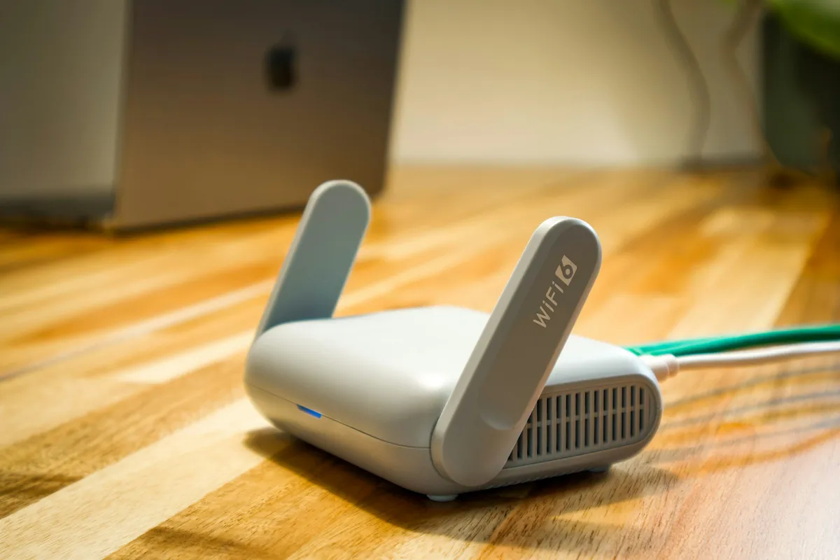 Roteador Wi-Fi com duas antenas sobre uma mesa de madeira, num ponto alto e afastado de eletrodomésticos como o micro-ondas