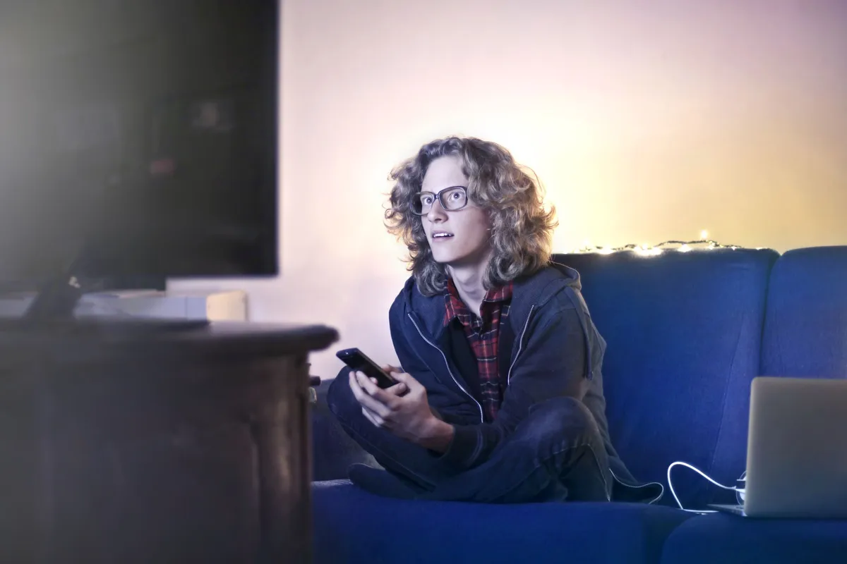 Pessoa usando o celular no sofá enquanto a TV está ligada ao fundo, exemplo de vários aparelhos usando a internet de casa ao mesmo tempo