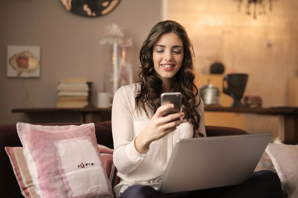 Pessoa usando celular e notebook no sofá em casa, exemplo de dispositivo que se beneficia do maior alcance da banda 2,4GHz