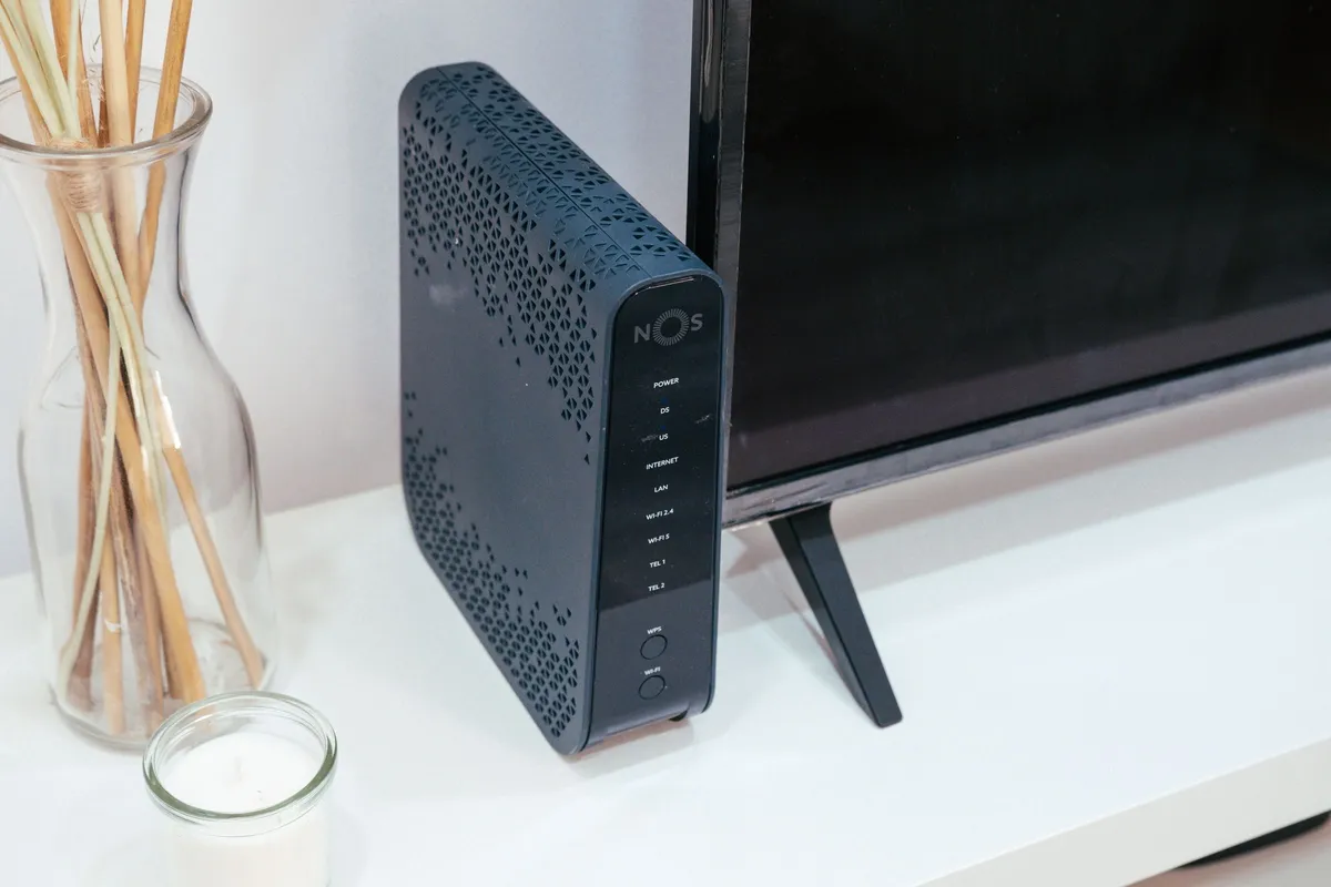 Roteador de Wi-Fi sobre o móvel da sala, ao lado da tela, exemplo de ponto da rede doméstica que o sistema mesh transforma em nó