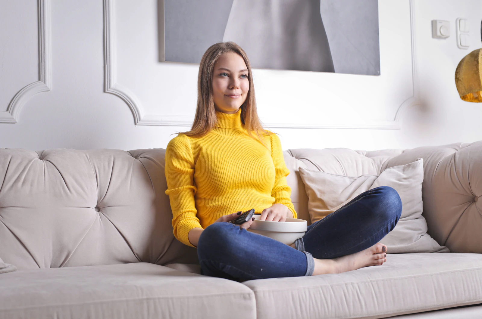 Mulher sentada no sofá com o controle remoto na mão, assistindo à TV em casa, exemplo de download: o conteúdo vem da internet até o aparelho