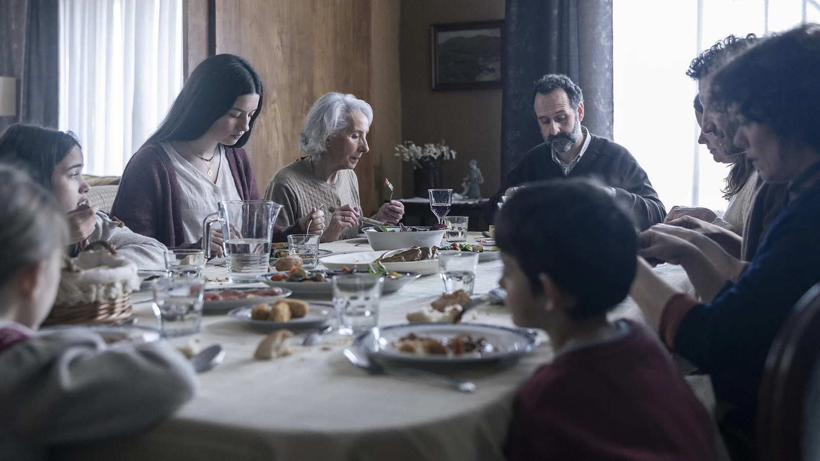 Família reunida em volta de uma mesa de almoço, com avó, pai, jovem de cabelo longo e crianças, cena do filme espanhol Os Domingos
