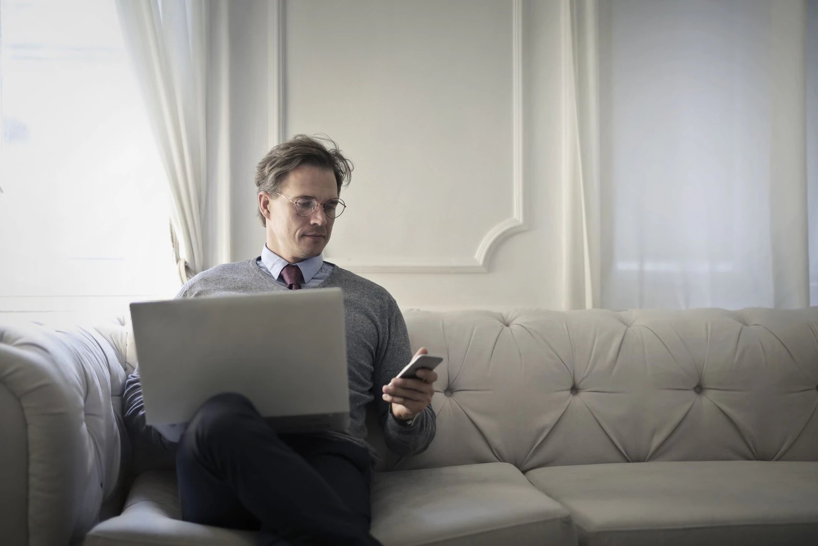 Pessoa sentada no sofá da sala usando notebook e celular conectados ao Wi-Fi de casa