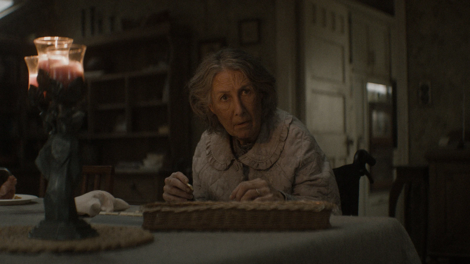 Senhora à mesa de uma casa antiga à luz de velas, cena de A Morte do Demônio: Em Chamas, sexto filme da franquia