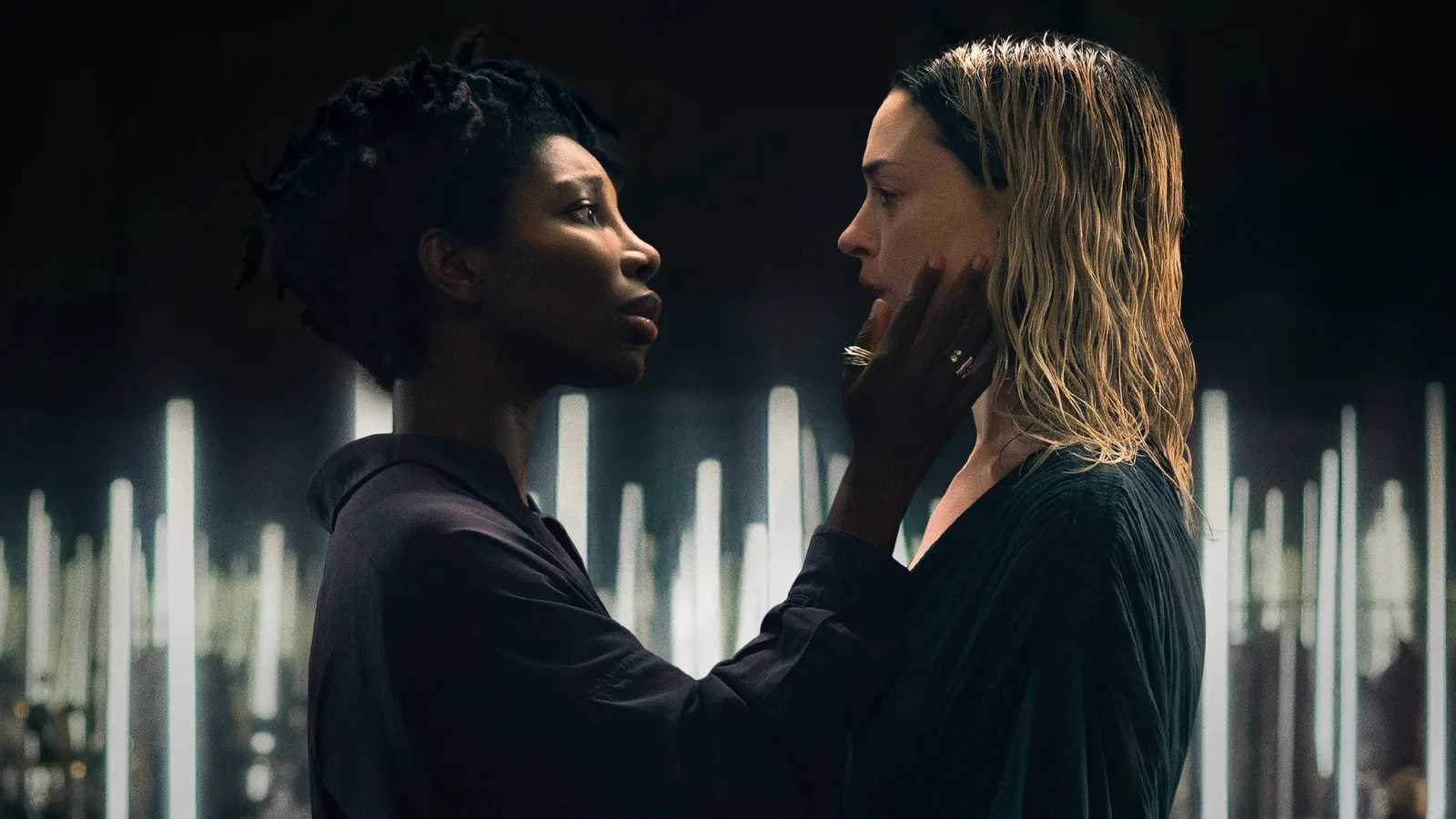 Michaela Coel segura o rosto de Anne Hathaway, de cabelo loiro molhado, as duas frente a frente diante de luzes brancas verticais, em cena de Mother Mary