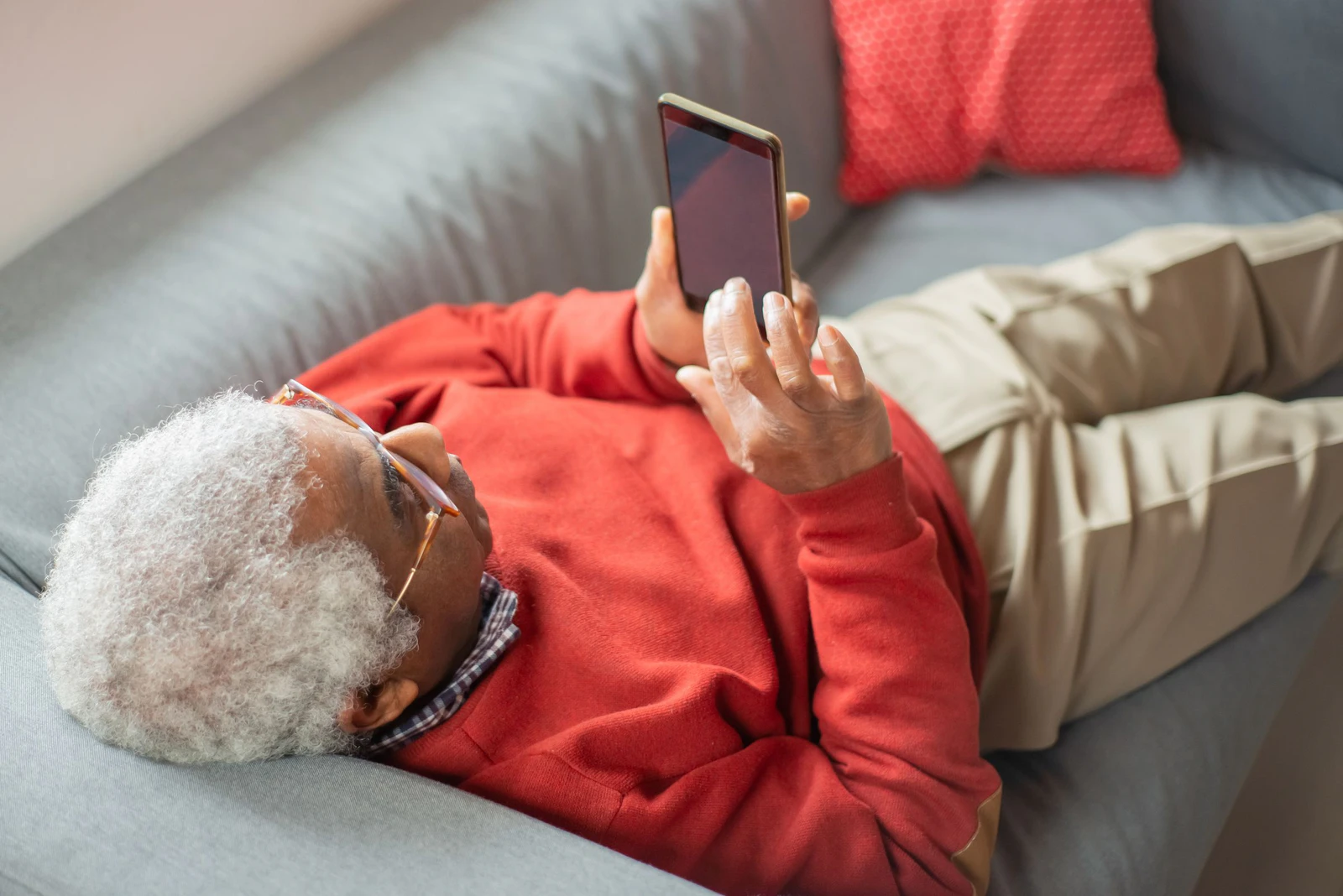 Homem adulto deitado no sofá usando o celular em casa, o tipo de uso em que o site ou o aplicativo abre pela internet