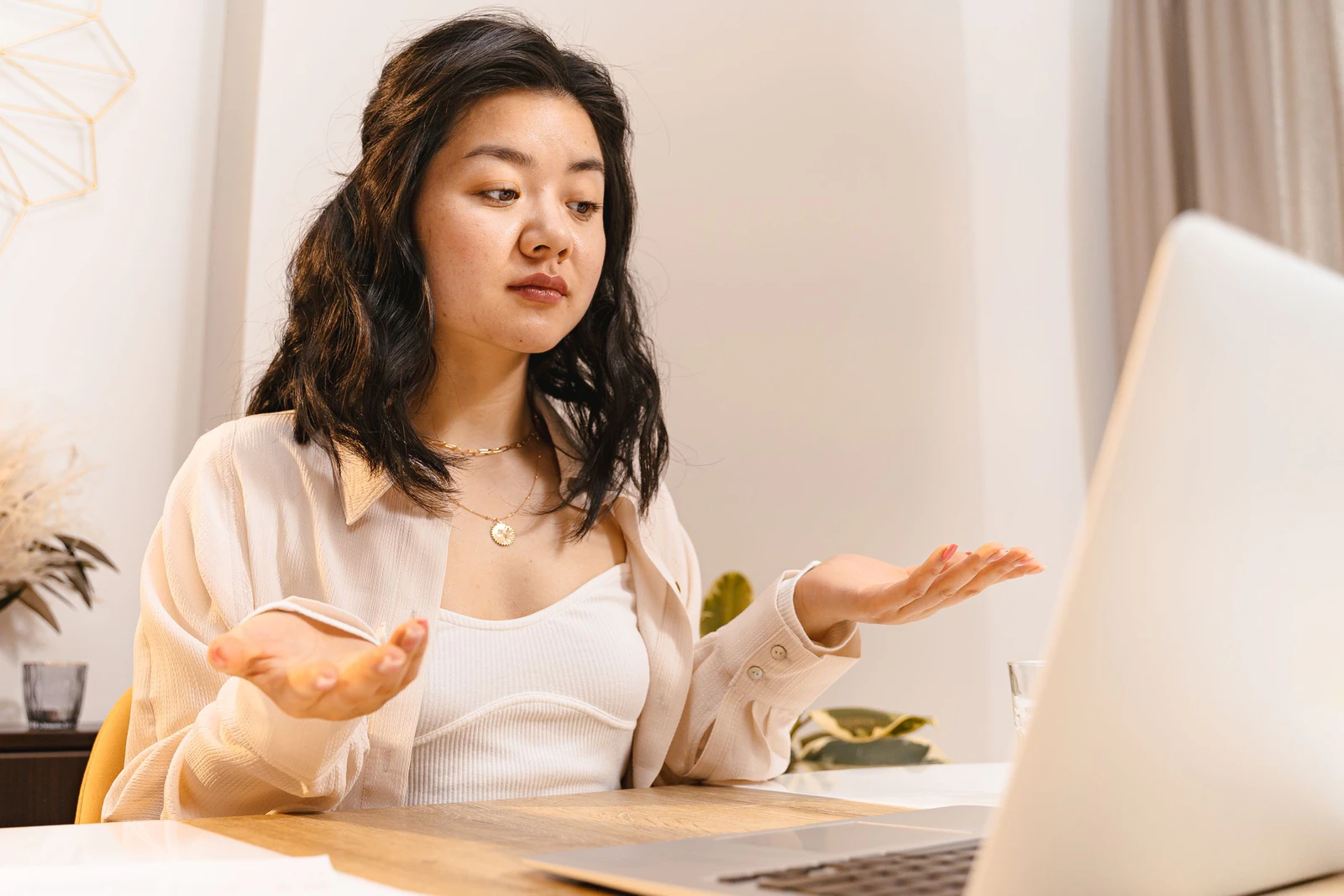Mulher sentada diante do notebook com expressão de dúvida e as mãos abertas, como quem não entende o que aconteceu na tela