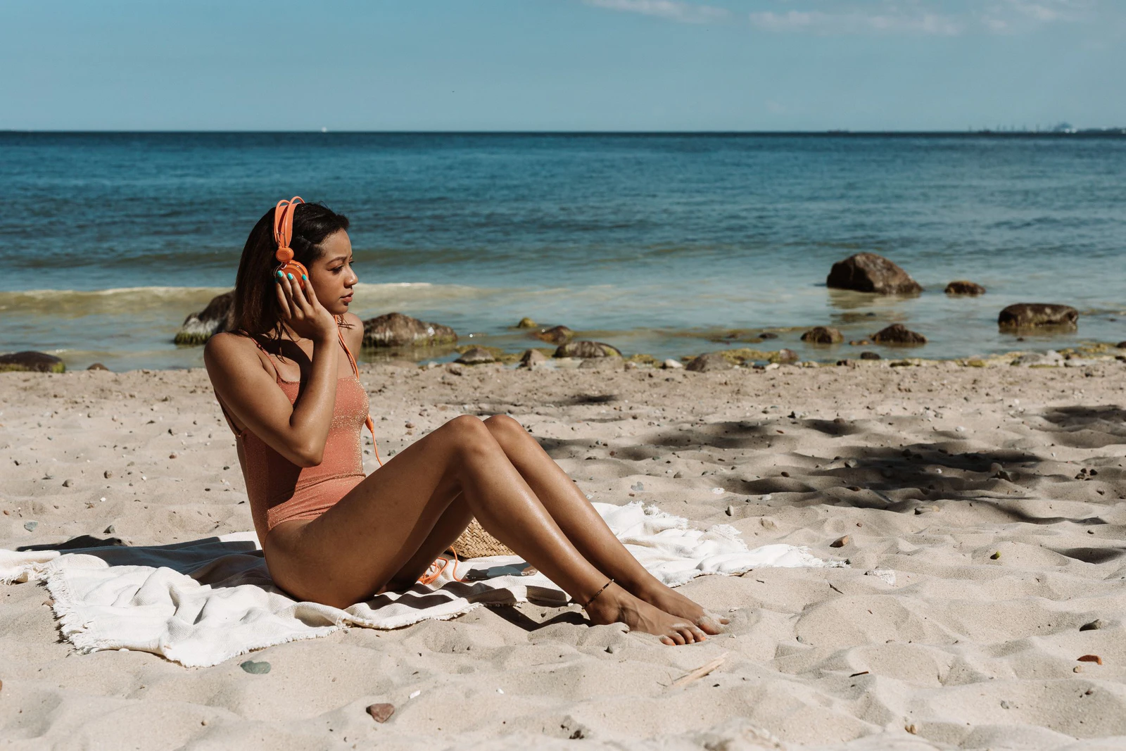Mulher de fones de ouvido sentada na areia da praia num dia de sol, ouvindo audiolivro sem gastar muita internet