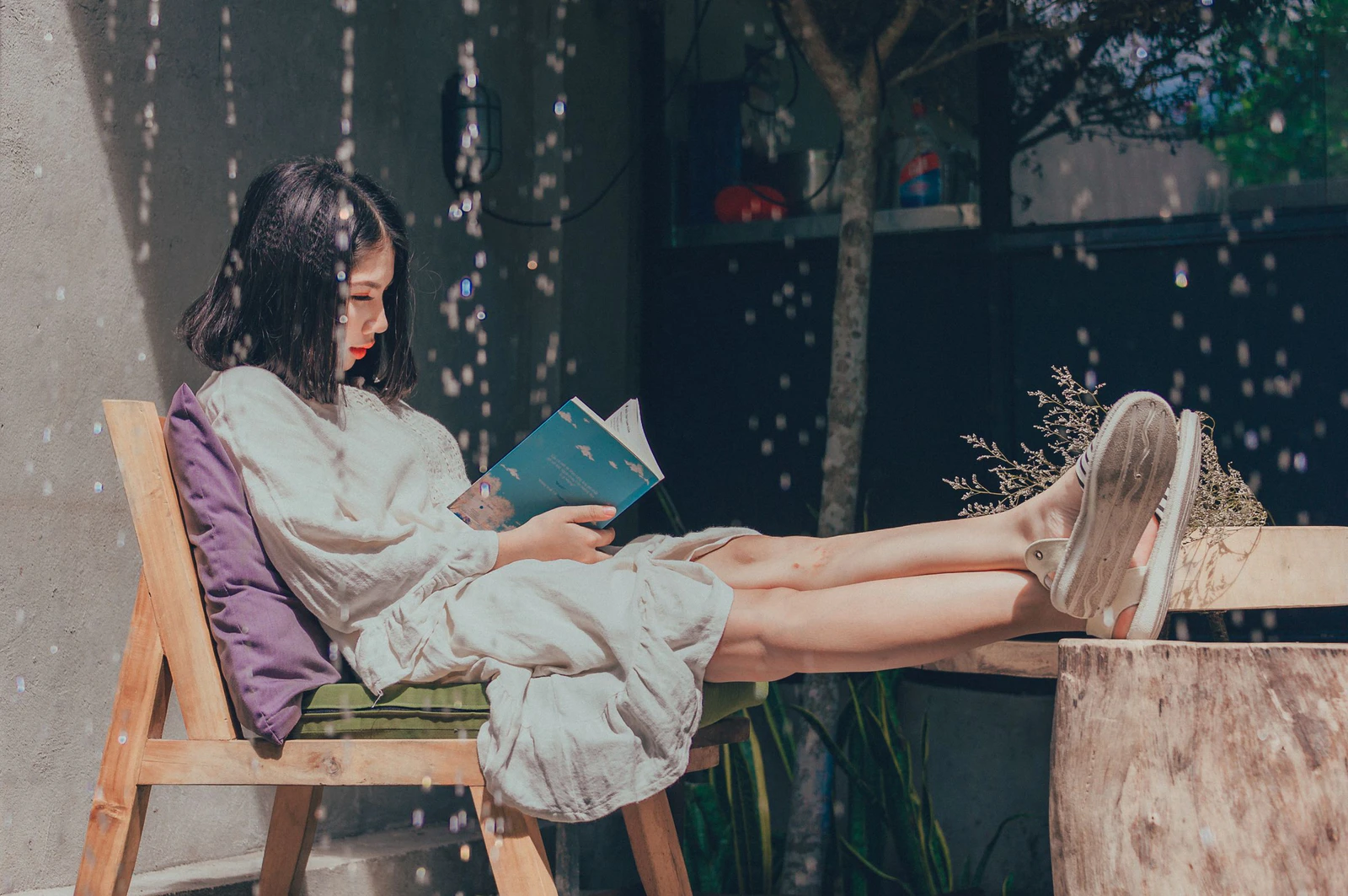 Mulher de vestido leve lendo um livro numa cadeira ao sol, cenário para o catálogo de audiolivros em português do Spotify