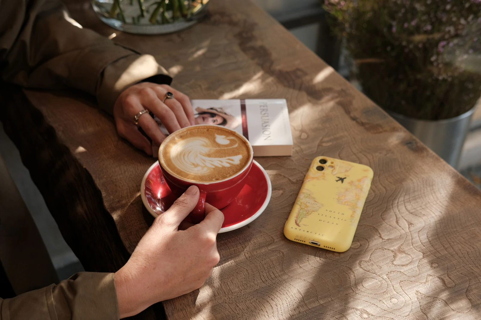 Celular, livro aberto e xícara de café sobre uma mesa de madeira, cenário para ouvir audiolivros no Spotify Premium
