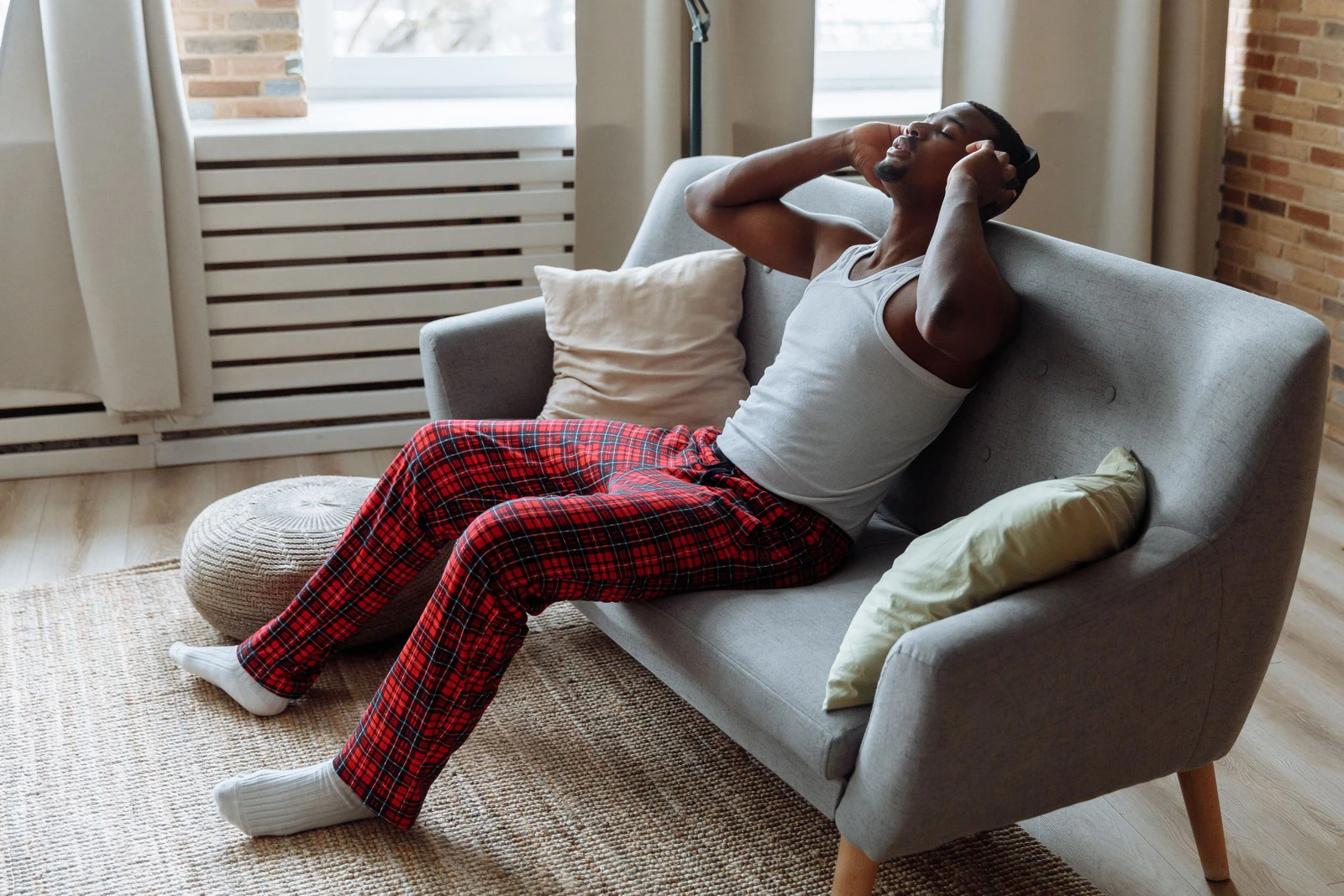 Homem relaxando no sofá de casa com fones de ouvido e olhos fechados, ouvindo um audiolivro