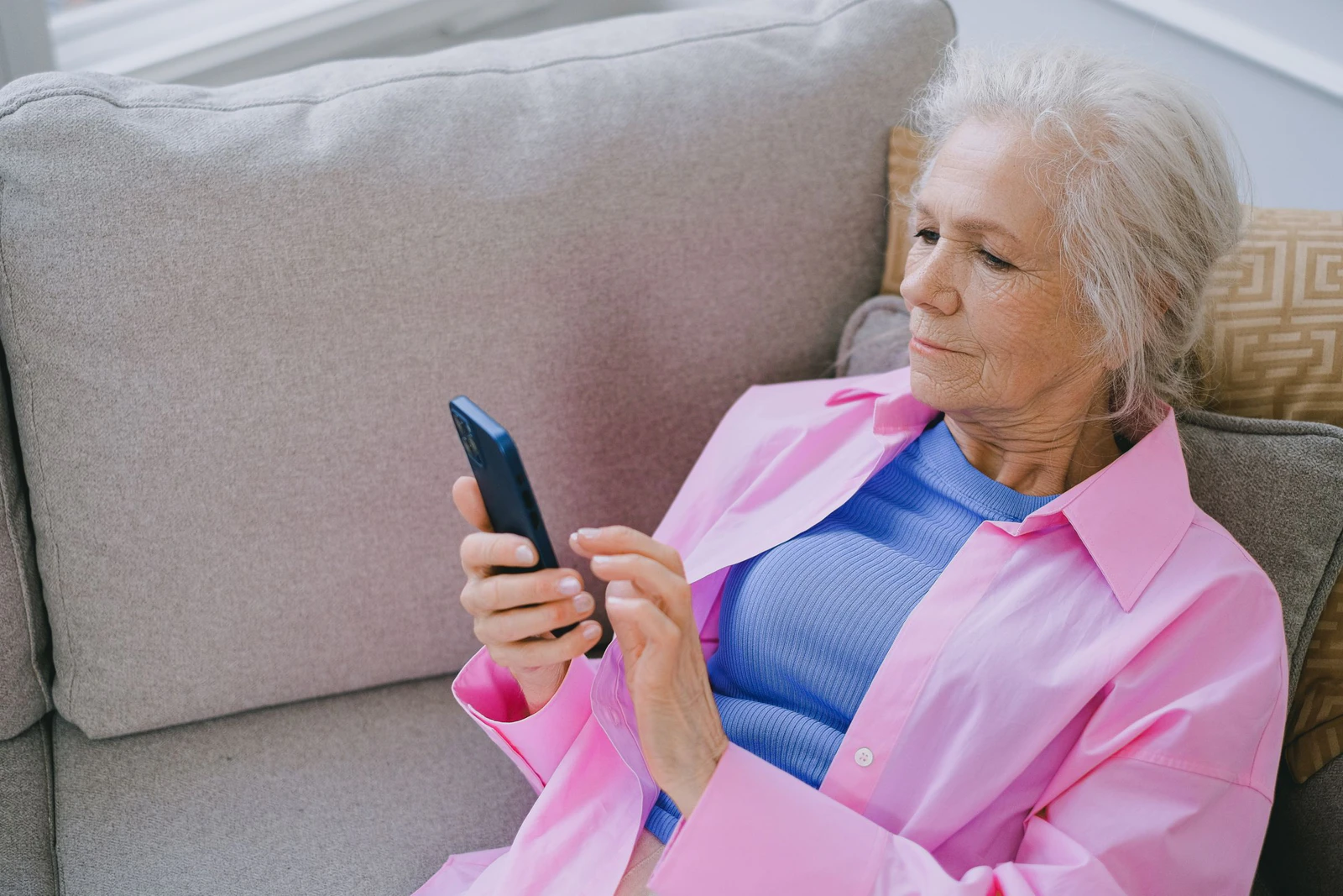 Mulher mais velha sentada no sofá usando o celular em casa